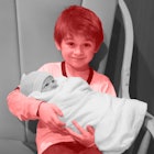 An older sibling with a red color filter holding his black and white newborn sibling in his lap