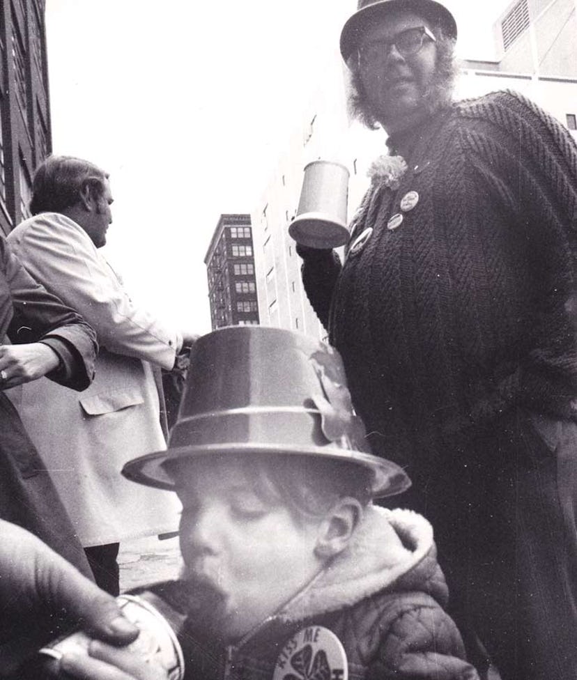 An old photo of a child drinking juice from a bottle and his father standing next to him and smiling