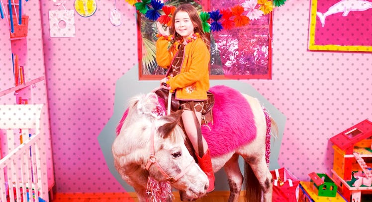 A girl sitting on a pink pony in a pink room