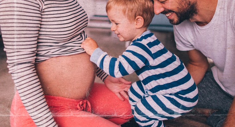 A dad, pregnant mom and their son sitting on the floor, the toddler is touching his mom's tummy
