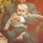 A dad in a blazer holding his child outdoors