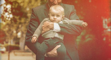 A dad in a blazer holding his child outdoors