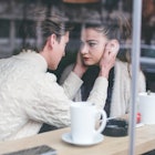 a man in a white sweater holds his wife's face and stares into her eyes at a cafe, a case of emotion...
