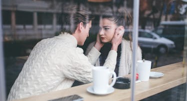 a man in a white sweater holds his wife's face and stares into her eyes at a cafe, a case of emotion...