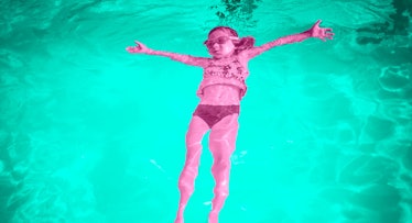 a young girl in goggles floats on her back in a bright aqua-green pool