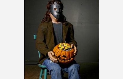 The Distortions Unlimited Candy Creeper sitting in a green chair and holding a carved pumpkin head w...
