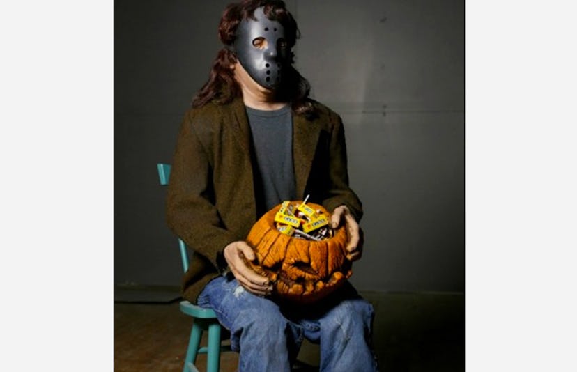 The Distortions Unlimited Candy Creeper sitting in a green chair and holding a carved pumpkin head w...