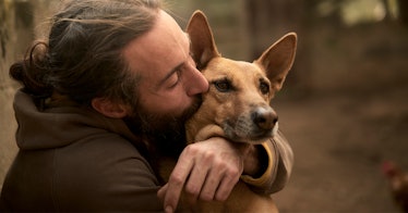 candid photo of a man with a beard hugging his dog and kissing him on the cheek