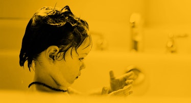 yellow tint edit of child with wet hair looking at their hand in the bathtub