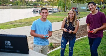 A woman and her two sons playing Mario Tennis outside