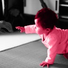 pink photo edit of a baby starting to crawl - against a black and white background.