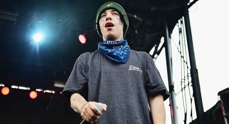 Lil Xan in a grey shirt, green beanie and blue bandana on his neck, performing on stage