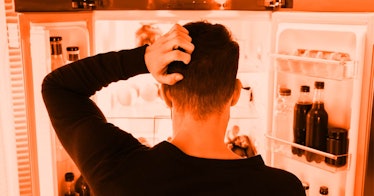 A man in a black shirt scratching his head while looking at an open fridge