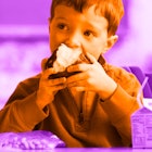 A little boy eating a muffin at school lunch