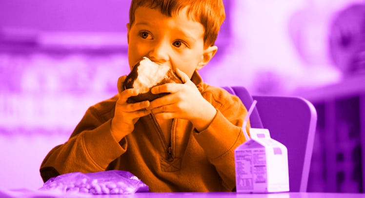 A little boy eating a muffin at school lunch