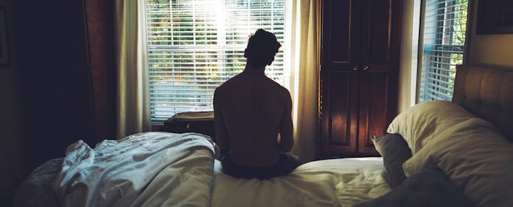 A boy sitting alone on his bed and looking through the window