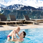 A smiling brunette mother holding her child in a swimming pool of a family hotel in the mountains