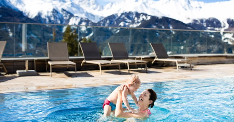 A smiling brunette mother holding her child in a swimming pool of a family hotel in the mountains