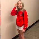 Instagram star Lil Tay standing in a red sweater and white shorts while moving her hair away from he...