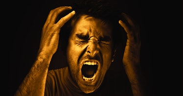 A man screaming in anger, grabbing his head. 