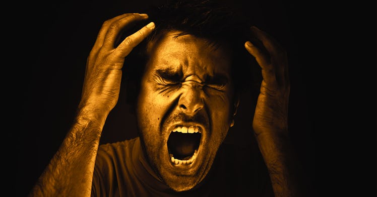 A man screaming in anger, grabbing his head.