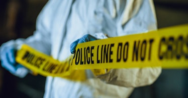 A police officer applying a yellow 'POLICE DO NOT CROSS' tape around a crime scene