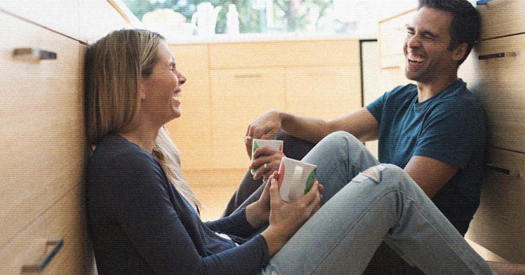 A couple in a happy marriage sitting on the floor of their kitchen with cups of coffee talking and l...