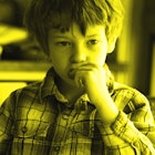 A kid sitting on a chair in the dining room eating a cookie in a plaid shirt. Yellow color filter