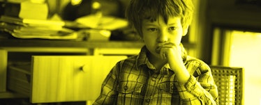 A kid sitting on a chair in the dining room eating a cookie in a plaid shirt. Yellow color filter