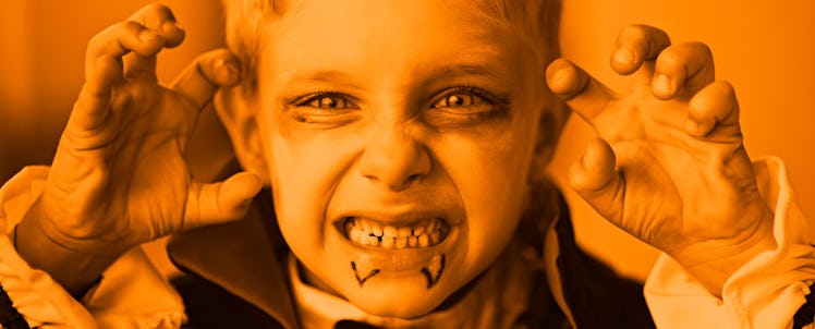 A close-up of a boy dressed up as a vampire for Halloween, trying to look scary with an orange color...