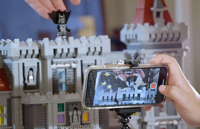 Father and son filming a stop-motion LEGO Batmobile scene with a mobile phone