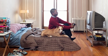 a man sitting on an unmade bed beside a dog, playing video games
