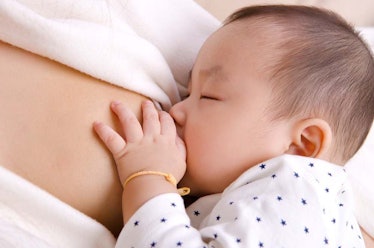 A mother in a white shirt breastfeeds her baby who is wearing pajamas with blue dots