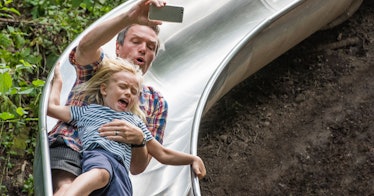 A father filming his time with his daughter on a park slide
