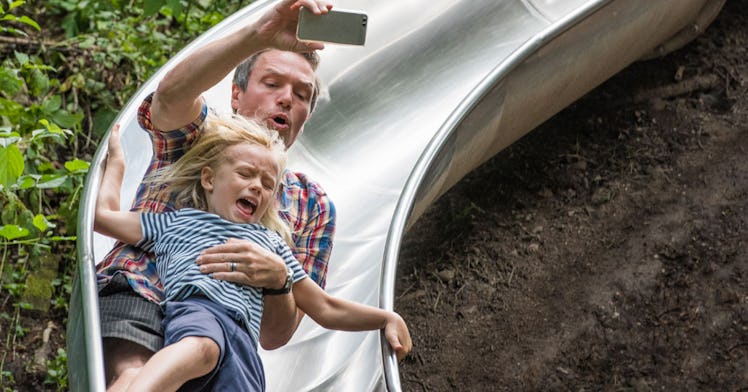 A father filming his time with his daughter on a park slide