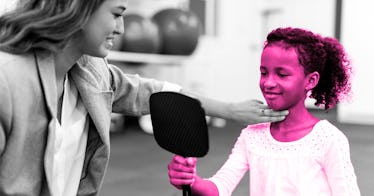 Child engaged in speech therapy looking at a mirror while speech therapist has fingers on her throat