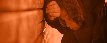 A 10-year-old wearing a winter coat leaning on a brick wall with his head on his hand