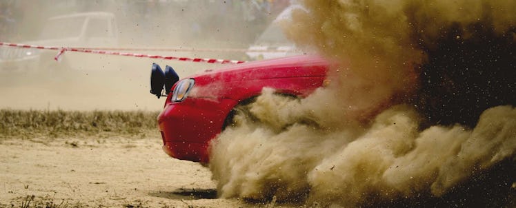 A red car covered with dust while driving through dirt