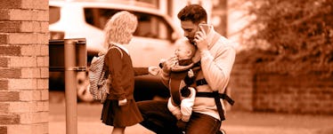A father talking on a phone while standing on a street with his two kids