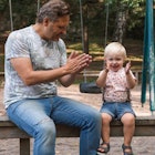 A dad and child on a bench at a playground clapping hands.