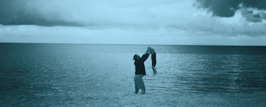 A man playing with his toddler whie they both stand in the water. Blue color filter