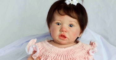 A brown-haired frighteningly realistic doll in a pink dress