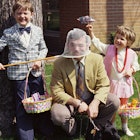 two kids holding easter baskets with dad in yellow suit crouching beside them telling easter jokes