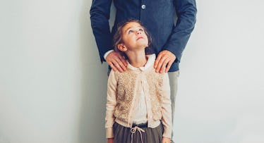 A little girl looking up at her dad who is holding her shoulders from behind in a supportive manner 