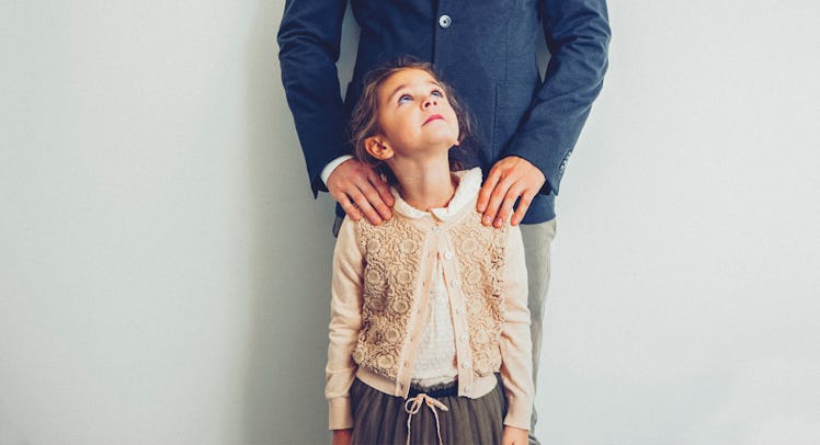 A little girl looking up at her dad who is holding her shoulders from behind in a supportive manner