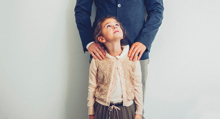 A little girl looking up at her dad who is holding her shoulders from behind in a supportive manner 