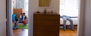 Two rooms separated by a wall. The dad is in one room laying on the bed, the mom is in the other roo...