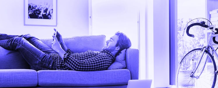 A man lying on a couch while using his tablet
