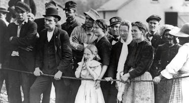 An old black and white photograph of a group of people standing behind a rope during the First Fathe...