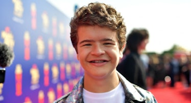 Gaten Matarazzo in a white shirt and black jacket smiling at a red carpet event
